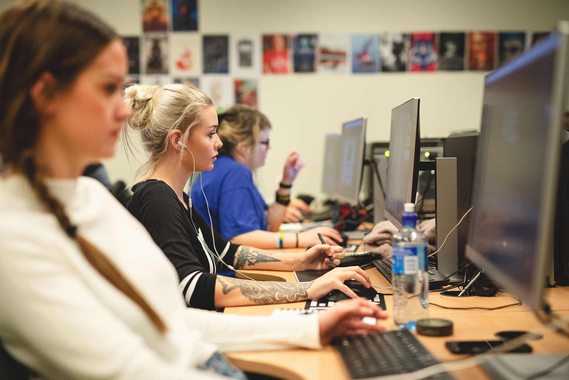 Foto av tre kvinnlige studenter som sitter i et klasserom og jobber på hver sin PC.