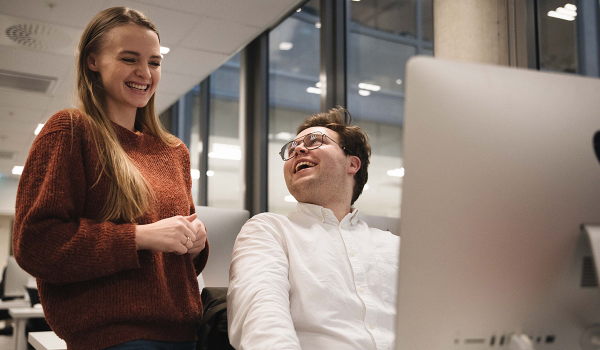 To studenter foran en iMac. De ler sammen.