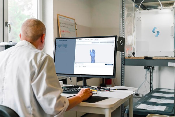 En man i hvit legefrakk sitter med ryggen til og ser på et dataanimert bilde av en hånd på en dataskjerm