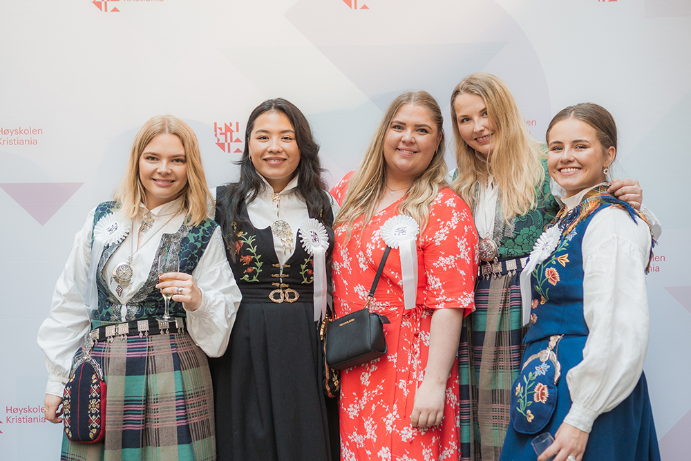Fem kvinnelige avgangsstudenter i kjoler og bunad smiler til kamera. Bildet er tatt under avgangsseremonien i Oslo i 2019.