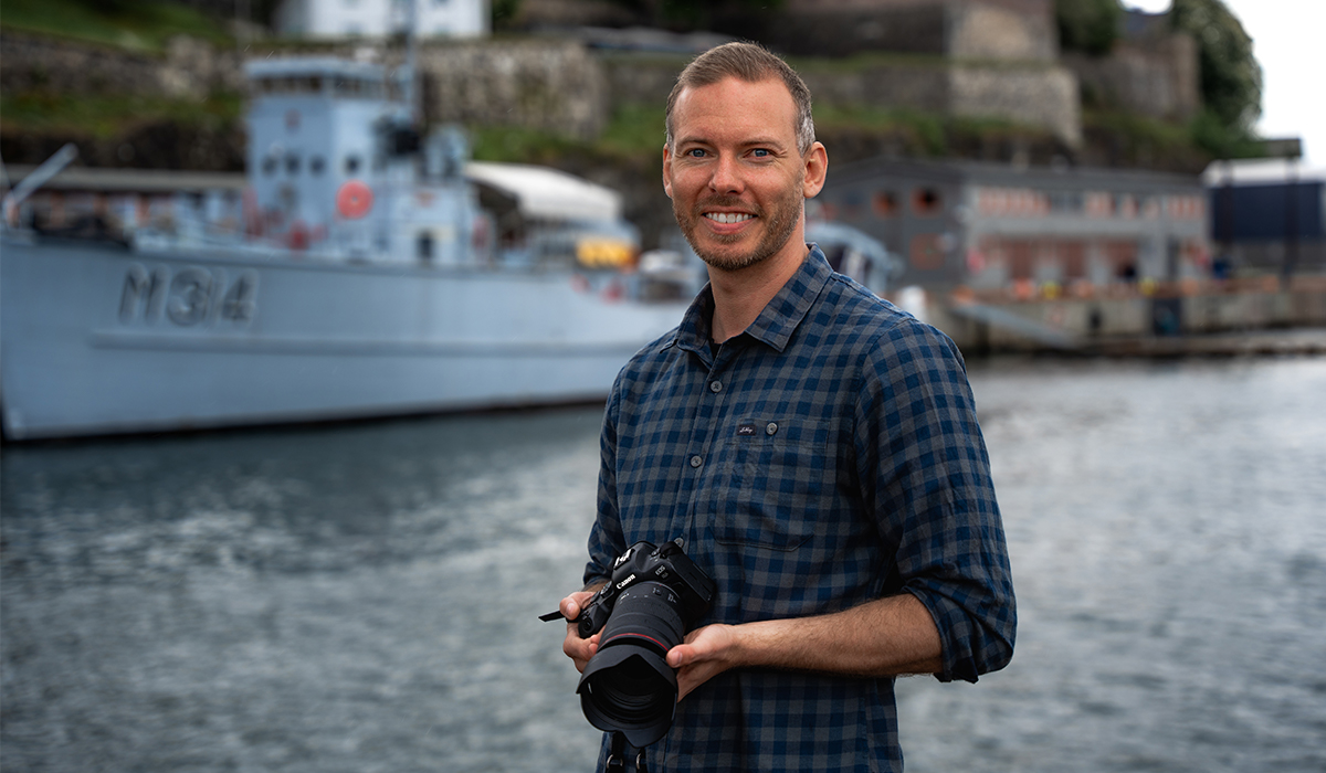 Foto av mann som står ute foran en båt og holder et kamera i hendene.