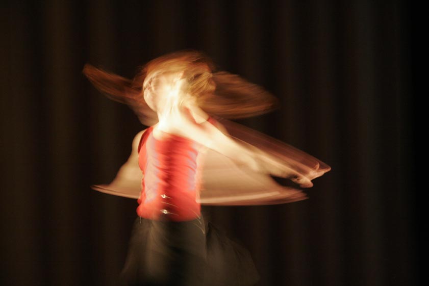 Hilde Rustad i improvisasjonsdans, fotografert kunstnerisk og litt uskarpt. Danser i rød topp og sort skjørt.