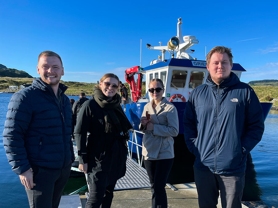 Foto av fire studenter foran en båt på besøk hos Grieg Seafood