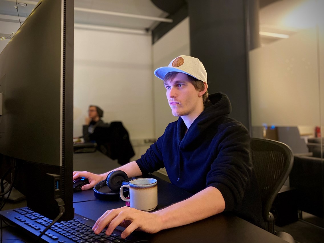 VFX-studenten Håkon som sitter foran en stor PC-skjerm og jobber med en kaffekopp