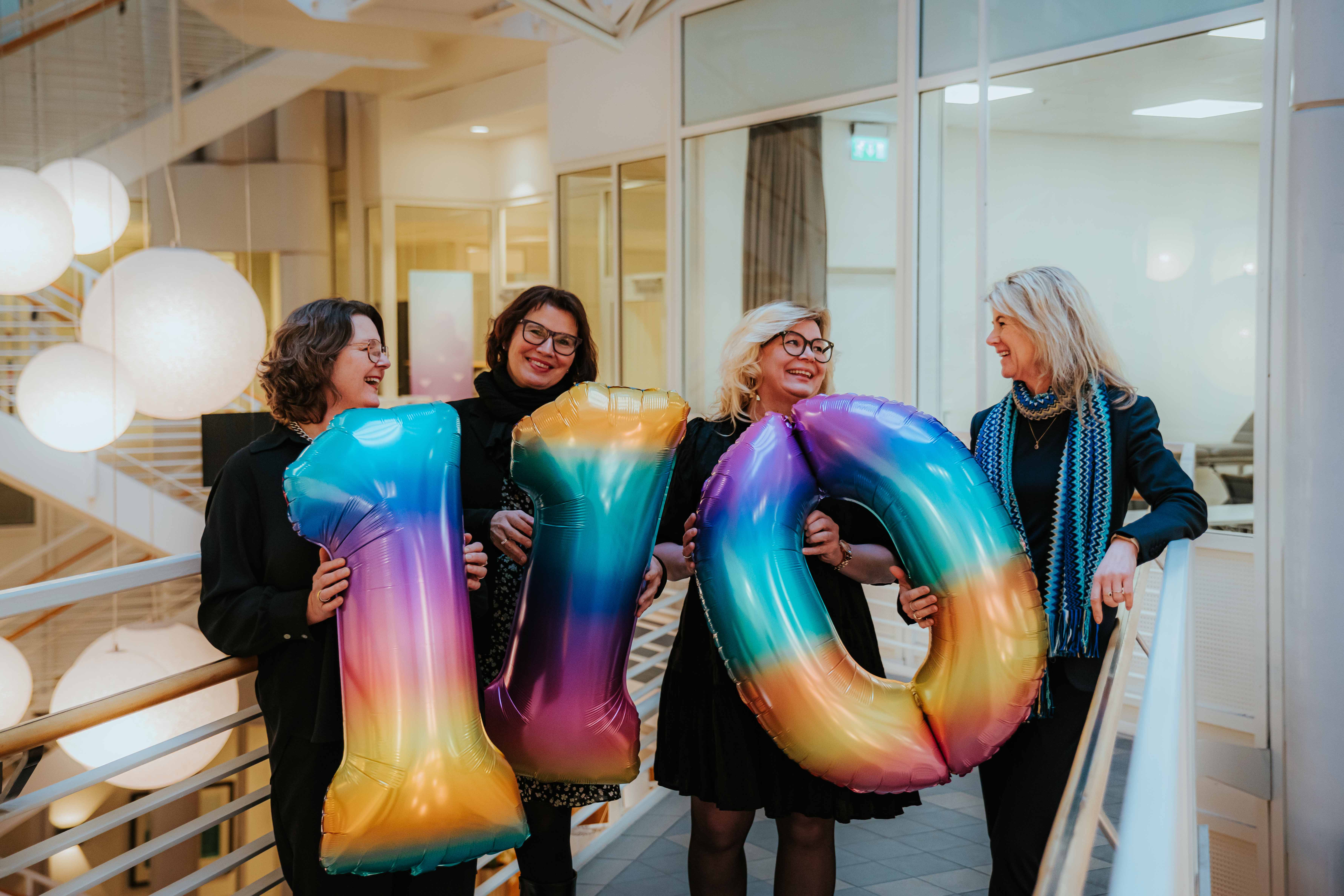 Fire kvinner står smilende og holder store ballonger som viser 110.